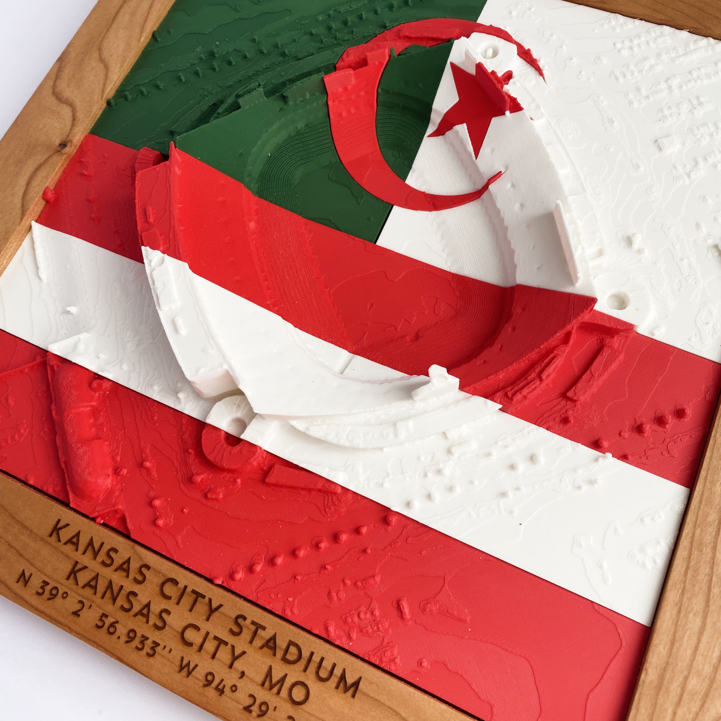 3D printed model of Arrowhead Stadium imprinted with Algeria's flag (solid green, solid white, with red moon and star) on the top half and Austria's flag (two red stripes with white stripe in between) on the bottom half - encased in a solid wooden frame engraved with the text "June 27th 2026; Algeria v Austria; Group J Kansas City Stadium, Kansas City, MO, and coordinates"
