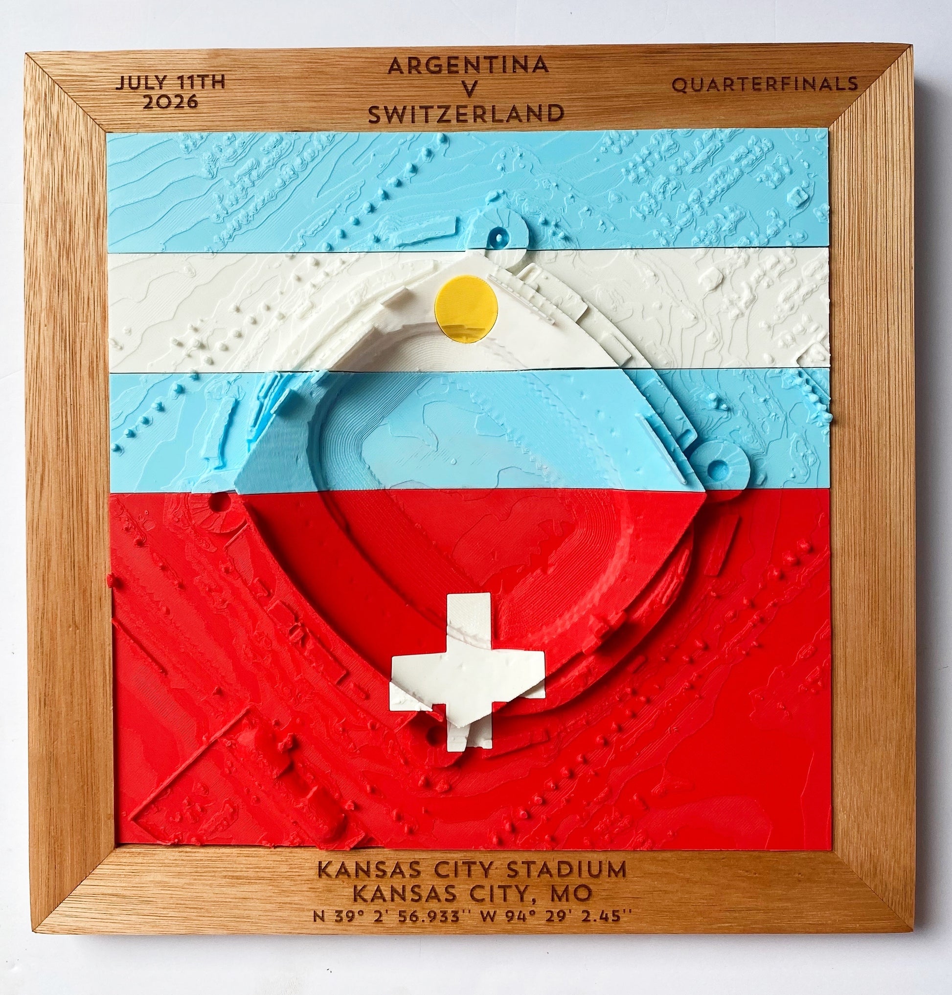 A square wooden framed wall art piece featuring a 3D relief map of Kansas City Stadium overlaid with the Argentina and Switzerland flag colors. The top text reads 'ARGENTINA v SWITZERLAND', 'JULY 11TH 2026', 'QUARTERFINALS', and the botto reads 'KANSAS CITY STADIUM KANSAS CITY, MO' with coordinates below.